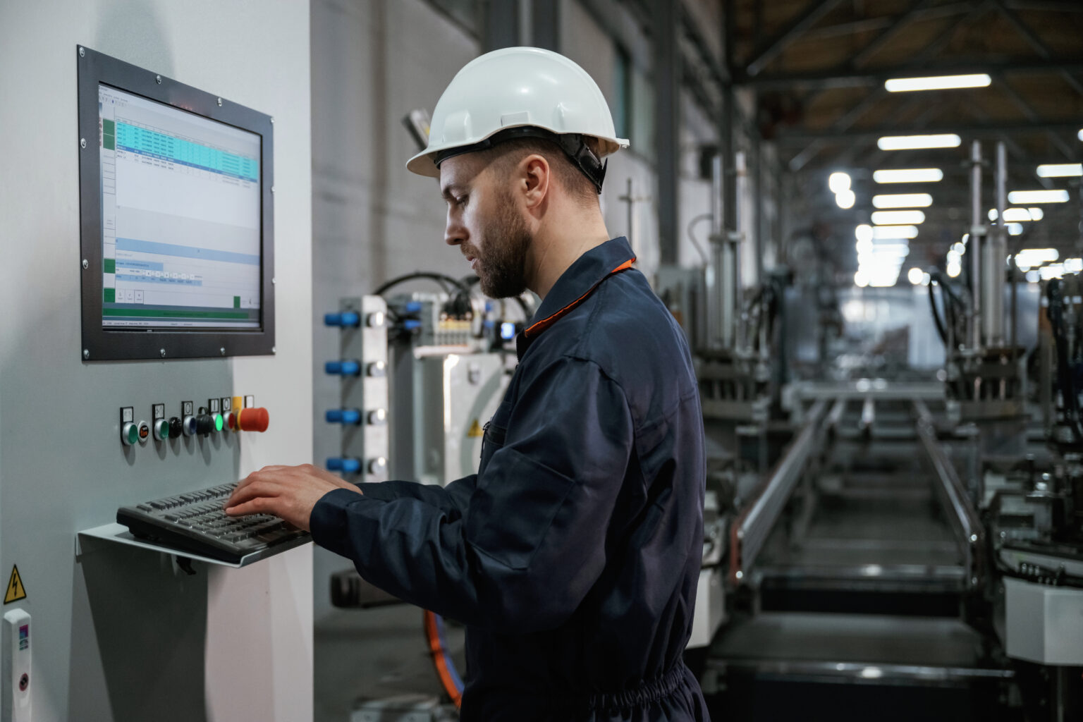 Adjusting settings of machine, operating. Factory worker is indoors with hard hat.